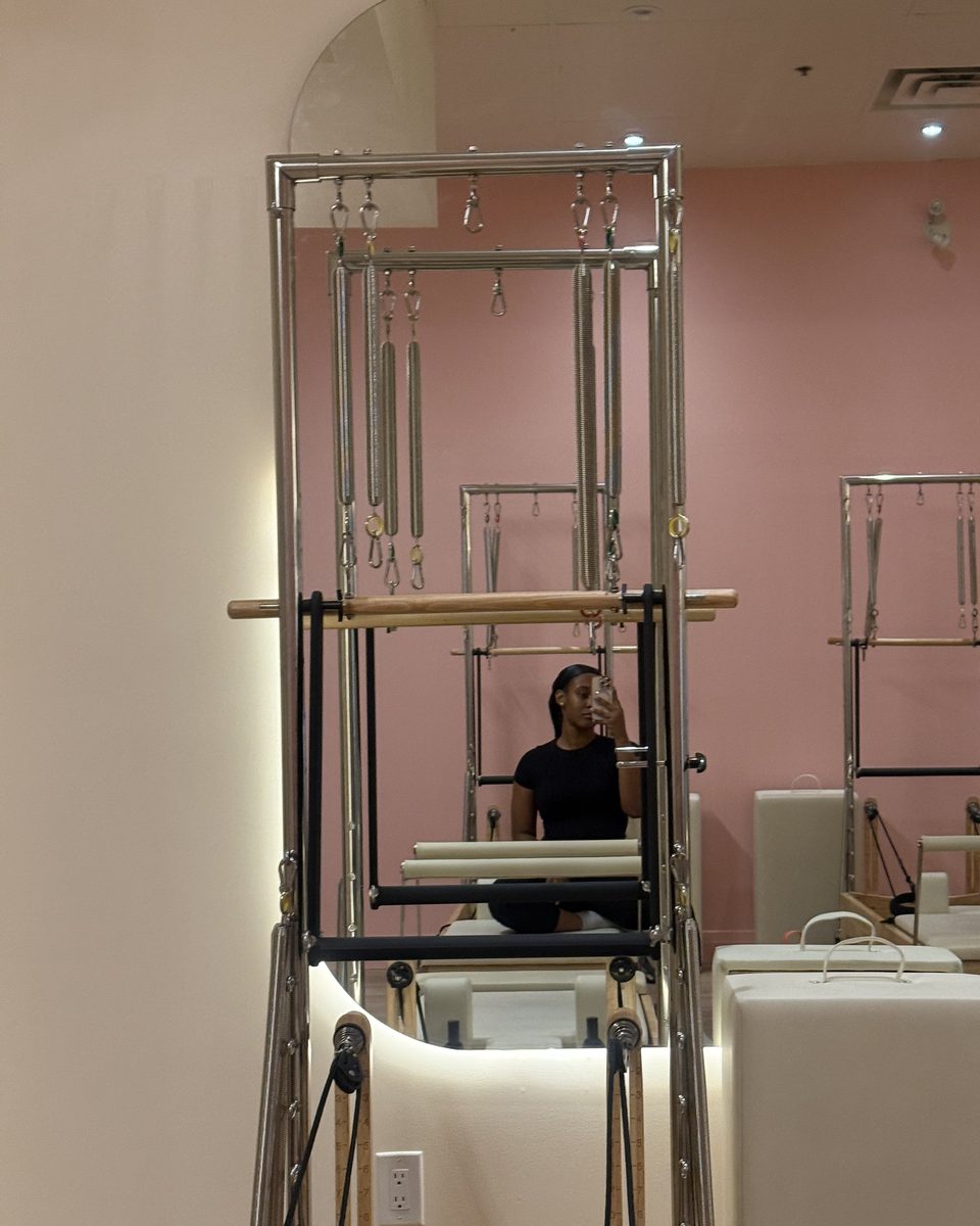Eys on a reformer in a pink Pilates studio, seen in the mirror